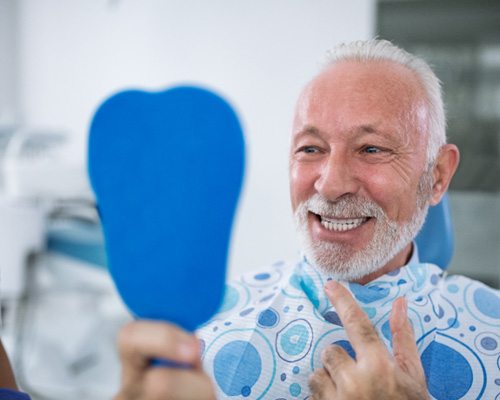 Male dental patient checking smile in handheld mirror